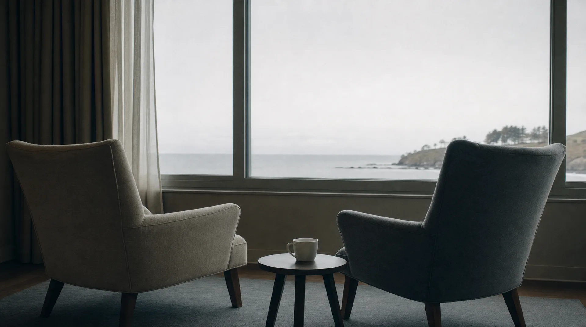 Two armchairs angled away from each other by a window, an untouched cup of coffee between them