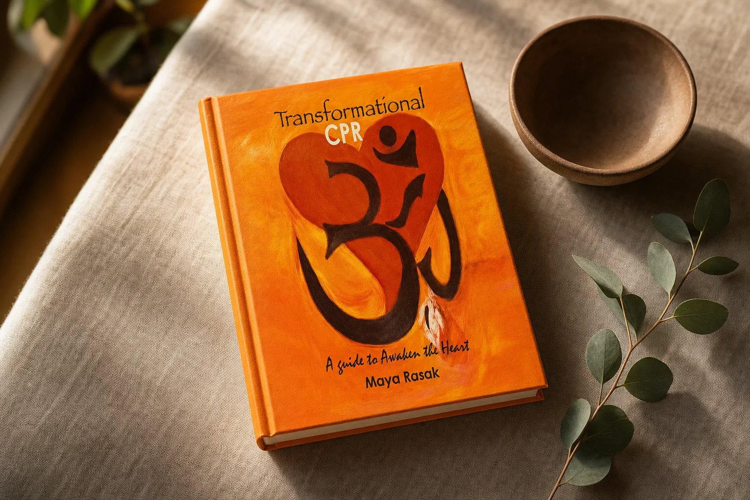 Transformational CPR: A Guide to Awaken the Heart by Maya Rasak, showing its orange painted cover with a heart and Om symbol, resting on linen beside a clay bowl